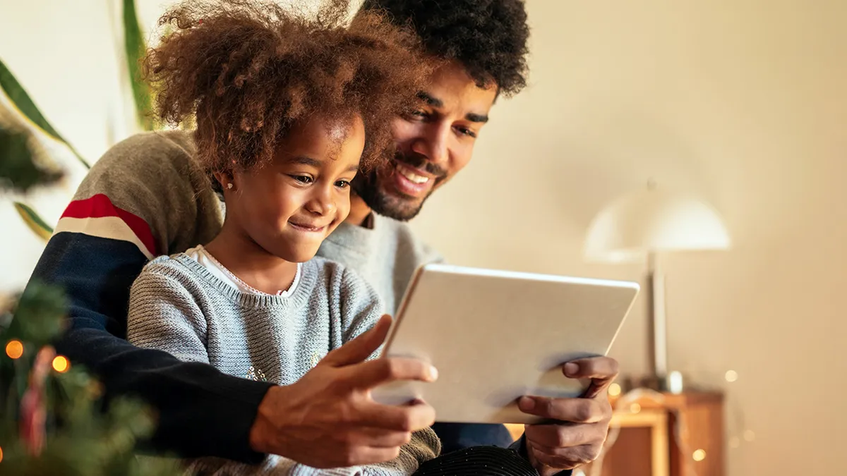 A child looking at a tablet in the arms of a parent with a christmas tree in the background