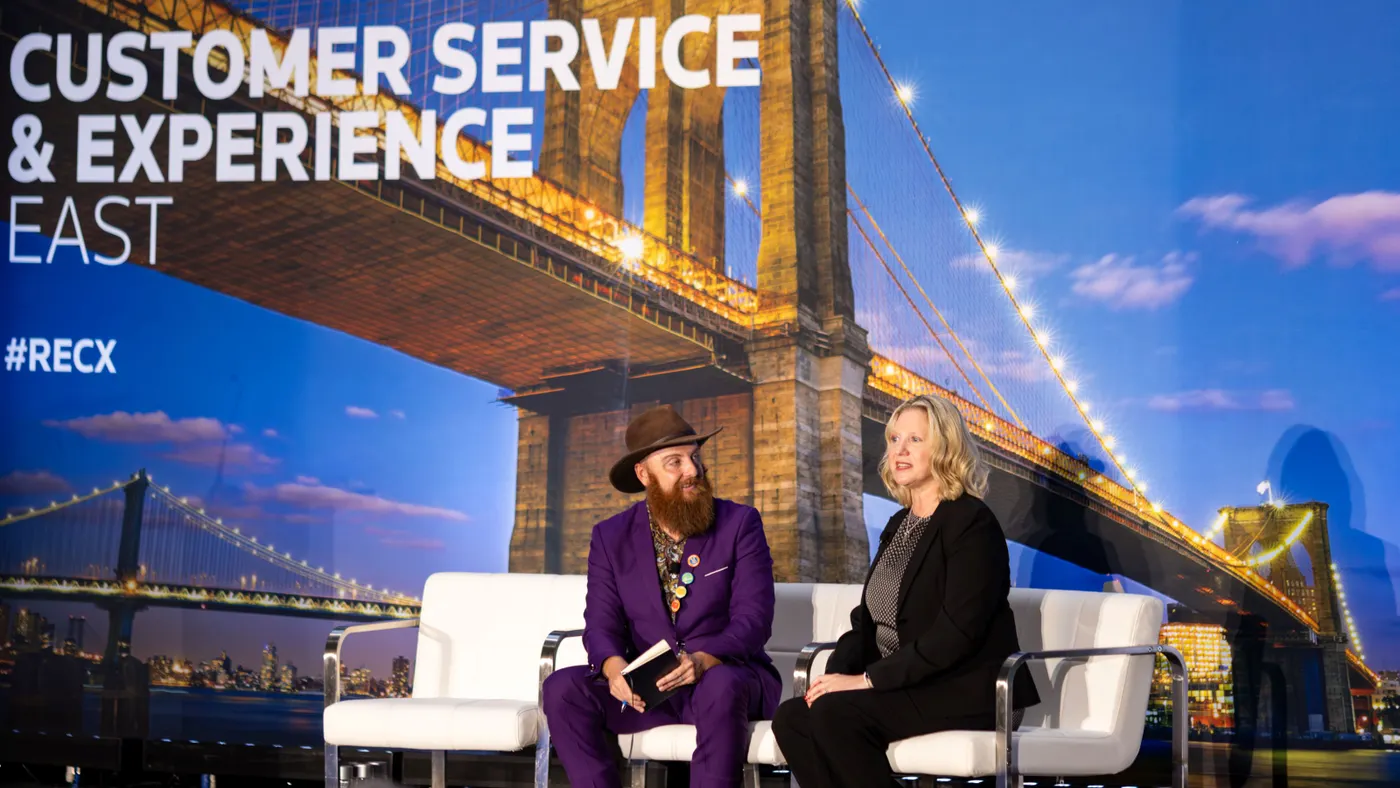 Two people sit on a stage for a fireside chat at a conference.