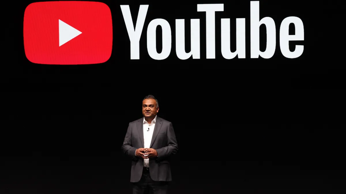 YouTube CEO Neal Mohan on a dark stage with the platform's logo behind him