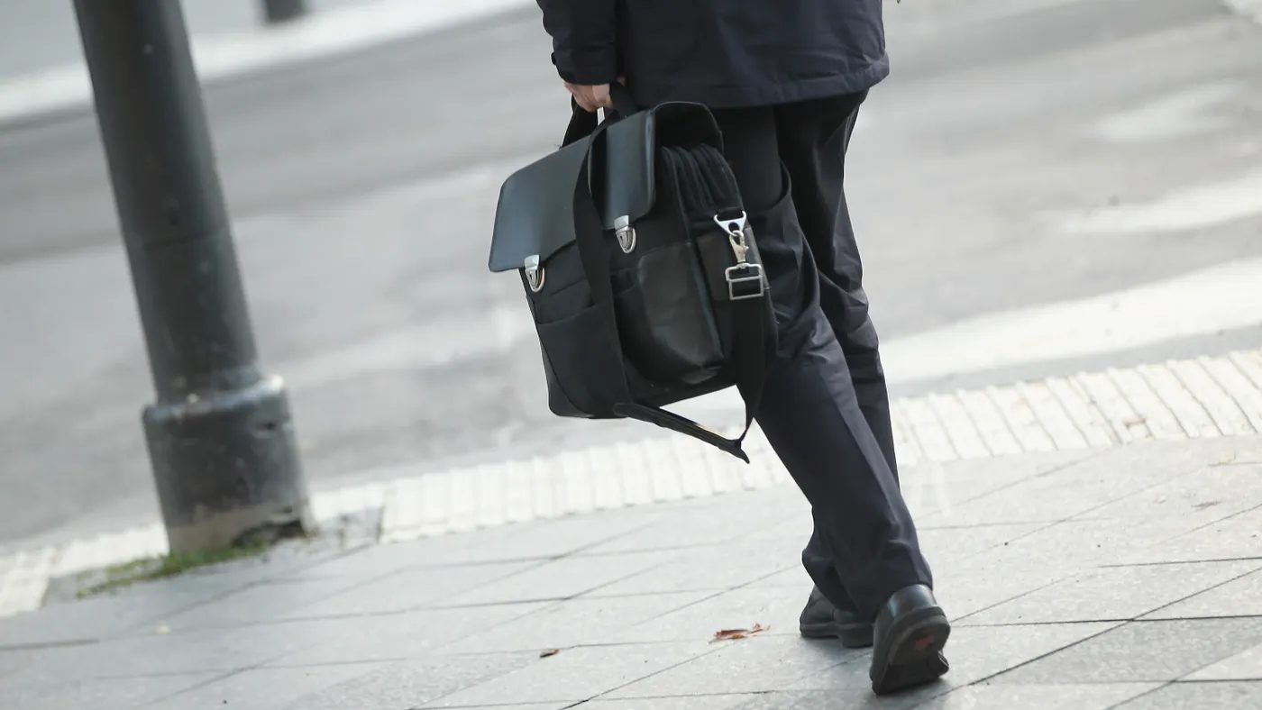Professional dressed in formal suit and shoes carries briefcase while walking down city street