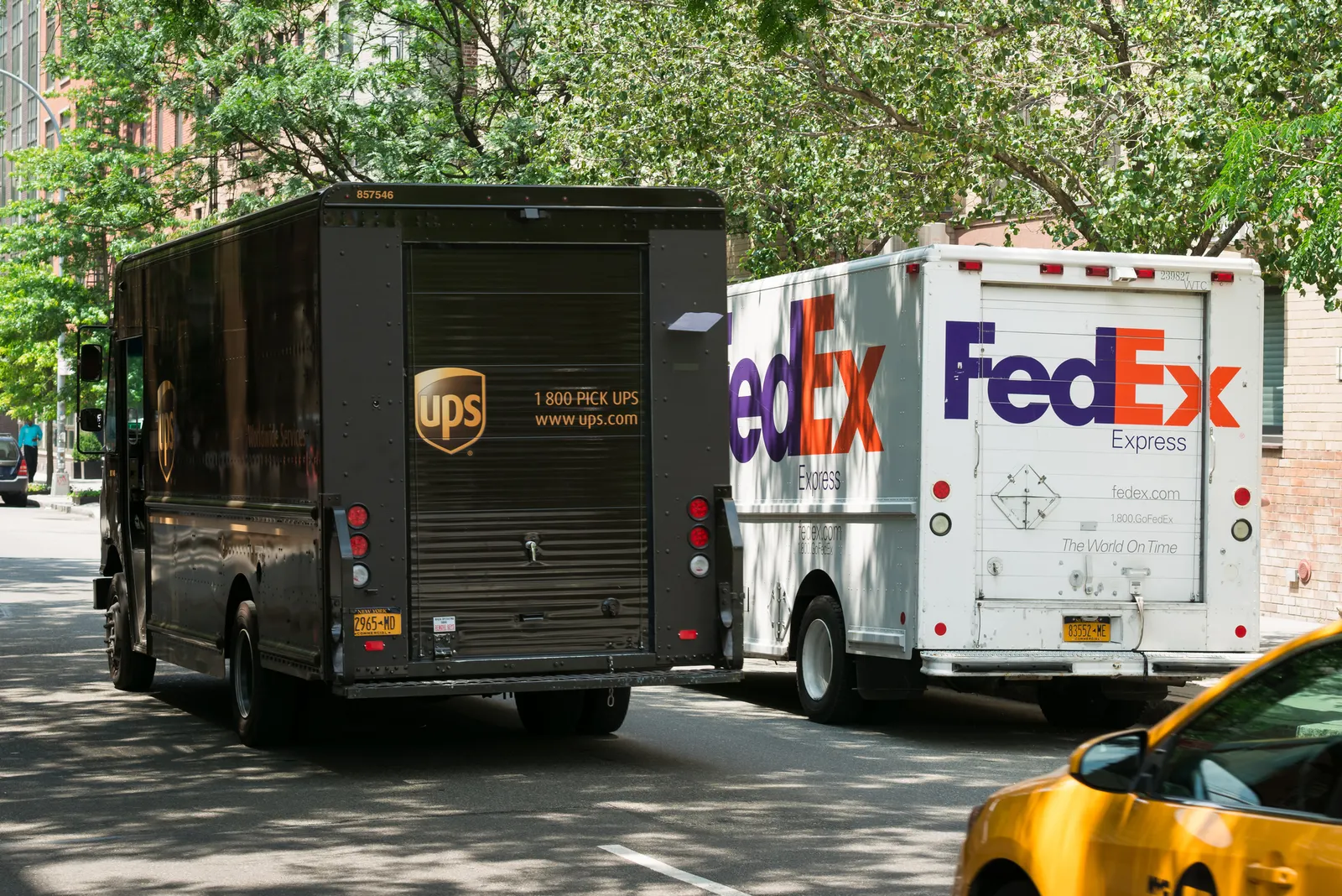 A UPS van passes by a FedEx vehicle on the street.