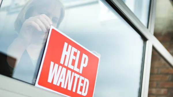 a woman hangs a Help Wanted sign on a window