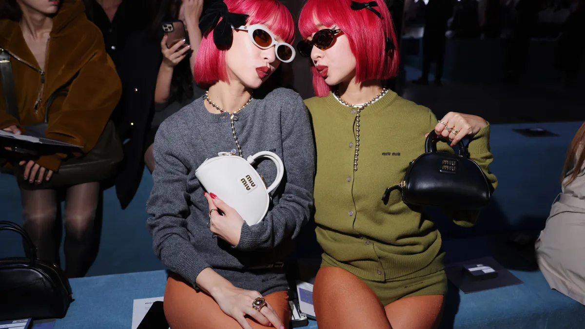 Japanese twin sister musician duo Amiaya pose in the front row of Miu Miu's spring-summer 2024 Paris show wearing the brand's logo cardigans and holding the brand's tiny handbags.