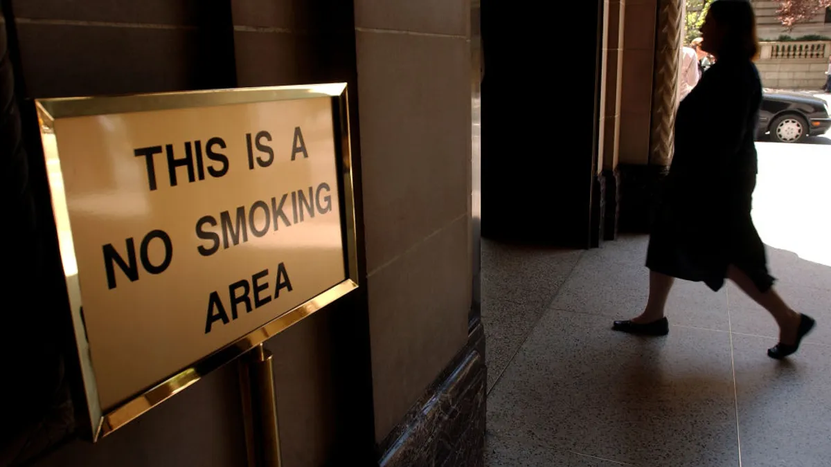 A person walks into a building with a sign out front that says "This is a no smoking area."