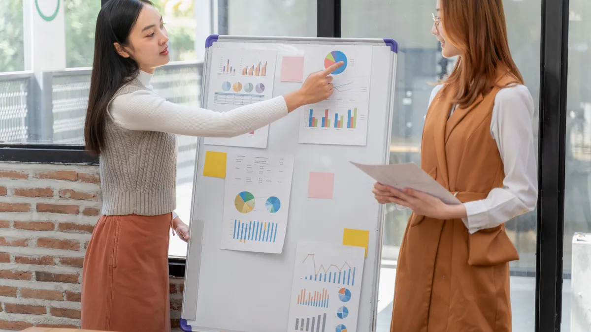 A high school student points to a business presentation while standing next to another classmate.