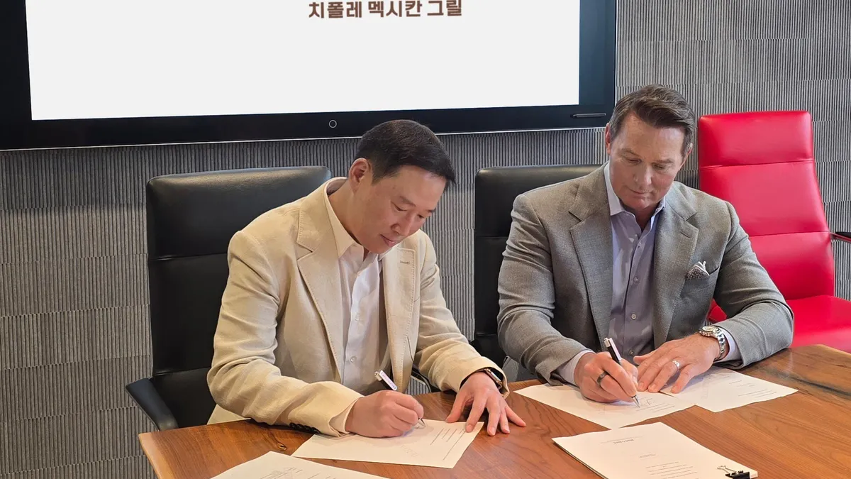 Two men in suits sign papers.