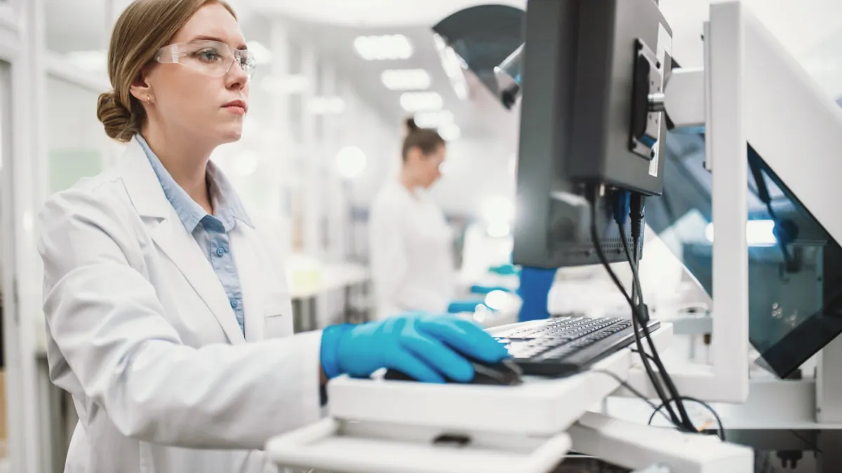 A team of laboratory technicians conduct a series of tests on a chemical analyzer in a biological laboratory.