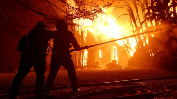 A pair of firefighters spray water on a burning home
