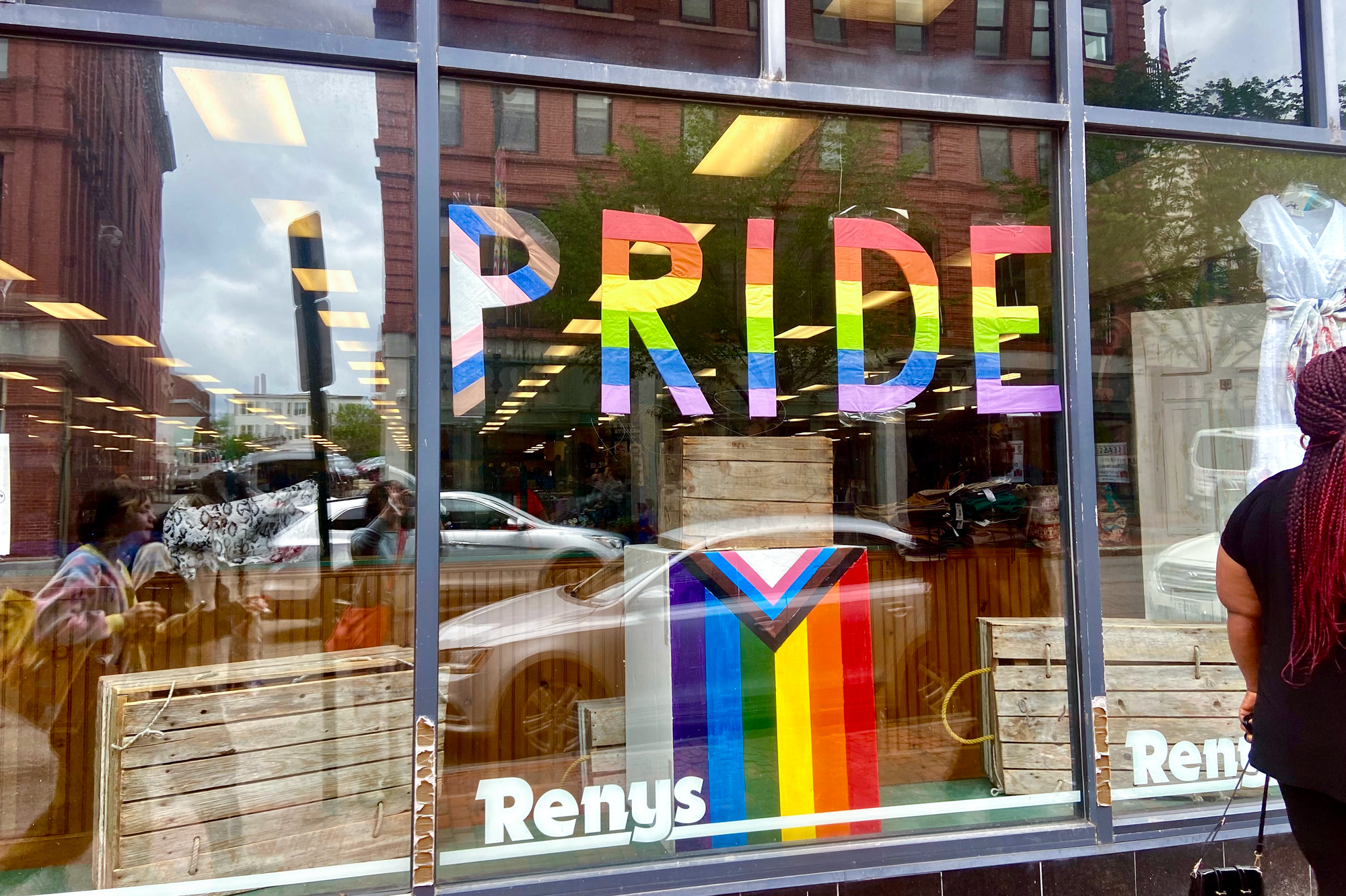 A shopper walks by a store window that is decorated for Pride Month with rainbow lettering.