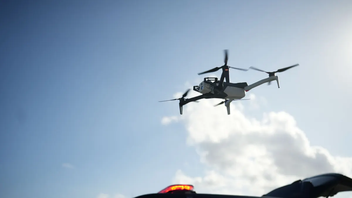A drone in the sky, flying over a black vehicle.