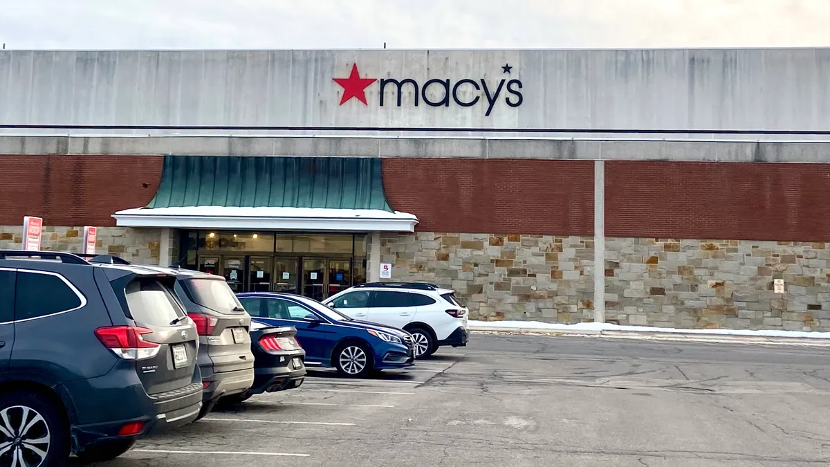 A row of cars parked outside a mall entrance to a Macy's store.