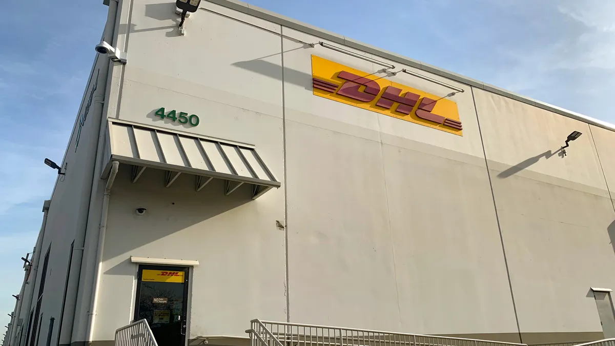 Corner entrance of a DHL facility building with steps and door and a blue sky in the background