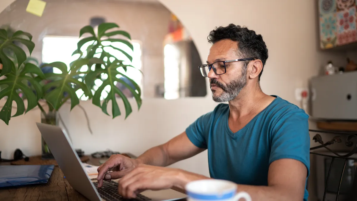 Greying, brown man uses laptop to work at home