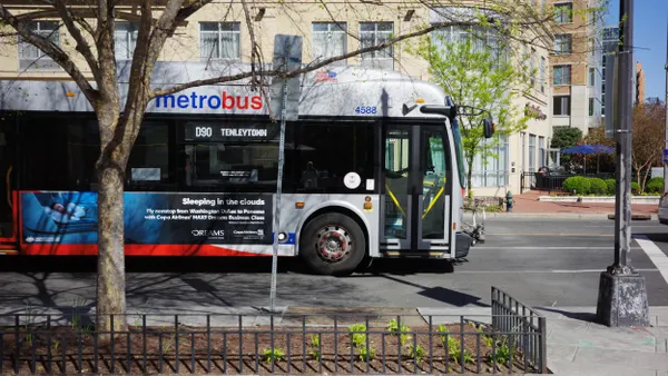 Side view of a transit bus lettered "metrobus" on a street with buildings behind it.