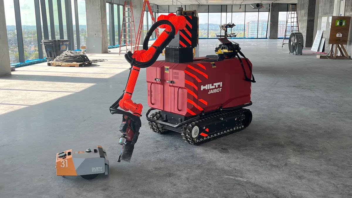 Two robots sit on a construction site on a DPR space. One is very small, the other is large and red.