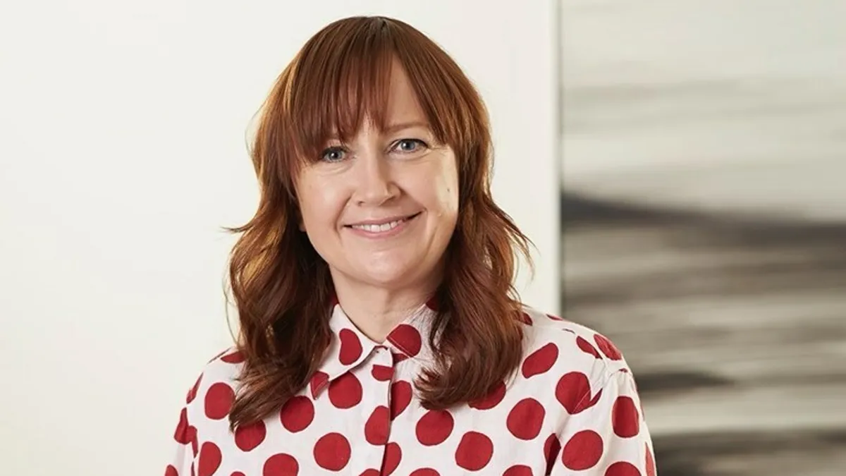 A person with long hair and a polka-dotted shirt smiles.