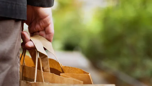 A hand holds a paper bag with thick handles