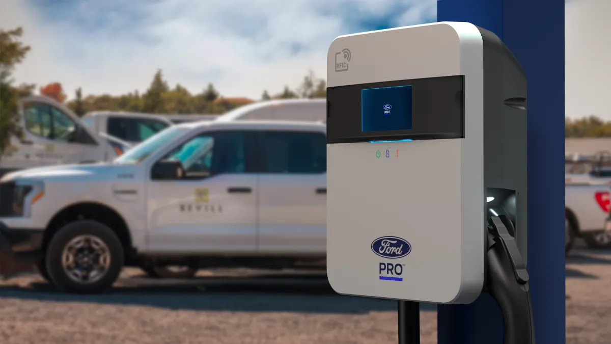 A Ford Pro electric vehicle charger with a F-150 Lightning pickup truck parked in the background.