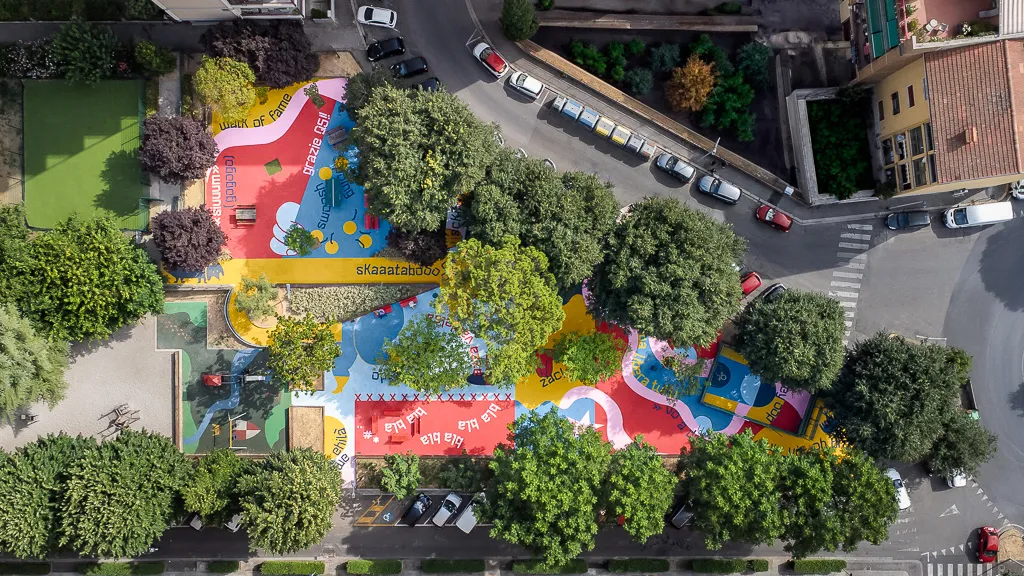 Aerial shot of triangular plaza with trees and bright murals on asphalt