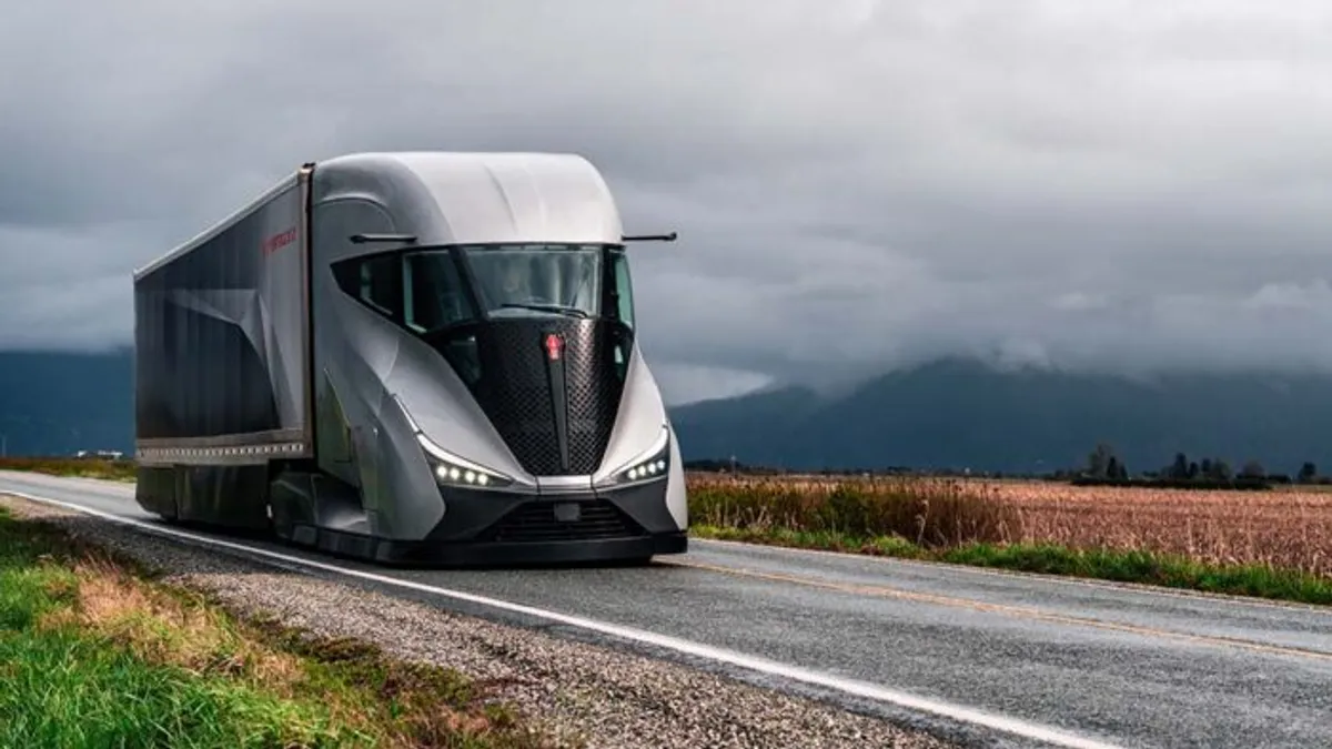 The Kenworth SuperTruck 2 on a road with clouds and a field in the background.