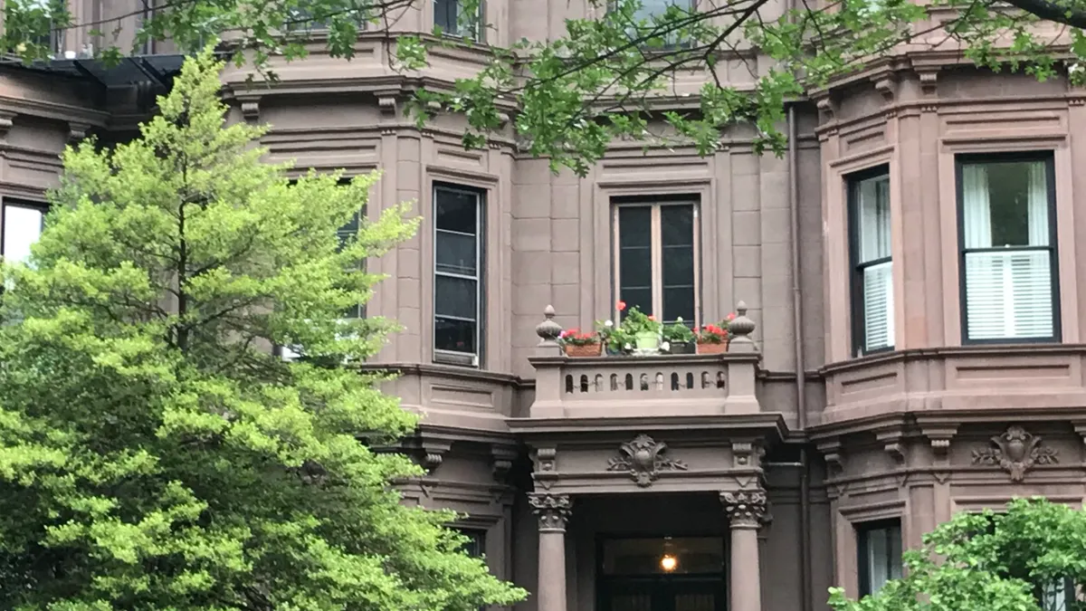 A three-story stone multifamily building with trees in the foreground