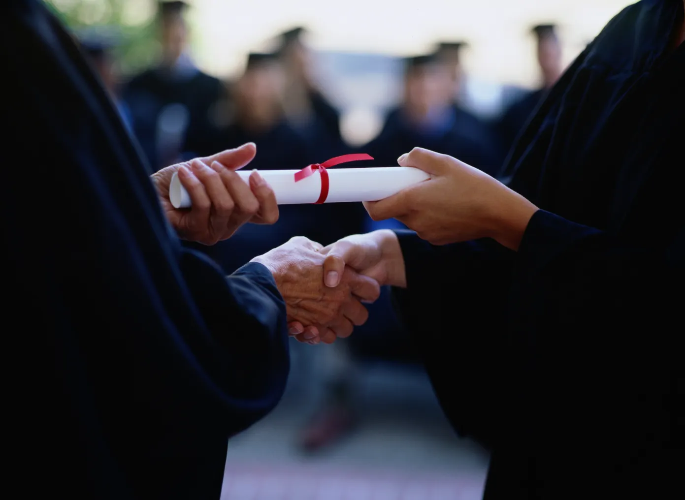 A close up of hands shaking, with one person giving the other a rolled up diploma