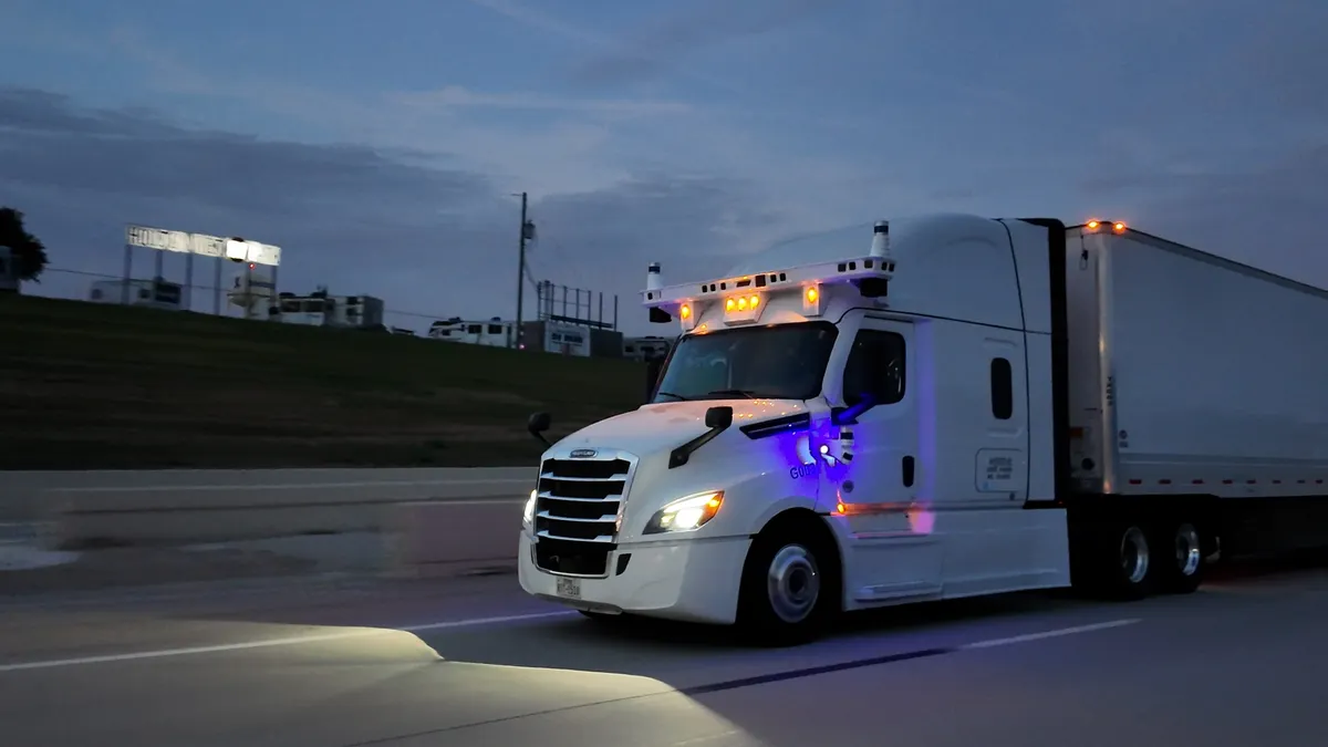 A driverless tractor-trailer equipped with autonomous technology moves along a roadway at dusk.