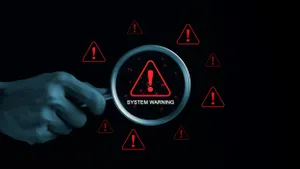 A hand holds a magnifying glass over a digital warning sign with red exclamation marks.