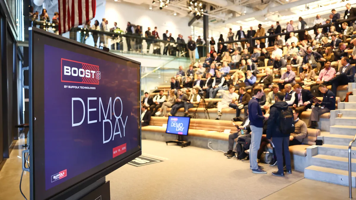 A group of people sit in an auditorium while a screen shows BOOST Demo Day in the foreground.