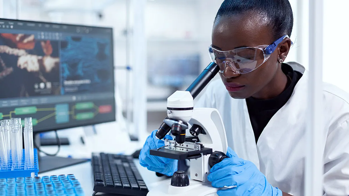 Medical researcher using microscope to evaluate a sample in a laboratory wearing sterile equipment