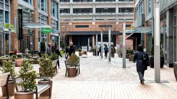 A photogrpah of a brick walkway with building and storefronts around it. There are a handful of people in the middle walking around.
