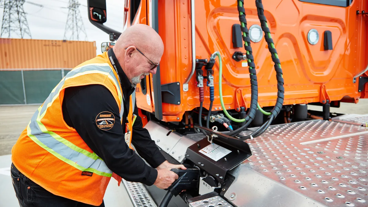 A Schneider National driver plugs an electric Freightliner eCascadia into a charger.