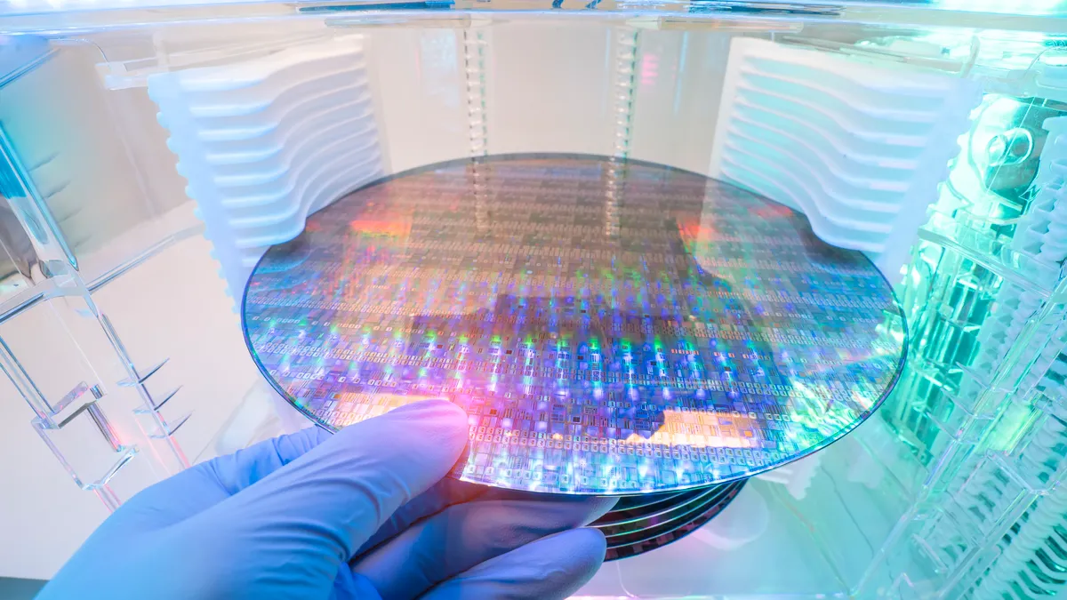 A blue gloved hand holding a silicon wafer in plastic holder box used in electronics for the fabrication of integrated circuits.