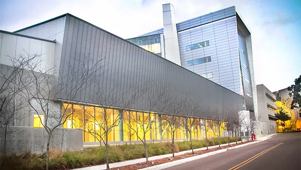 A shot of a building's exterior along a paved road. The modern looking building, covered in glass, looms in the photo.