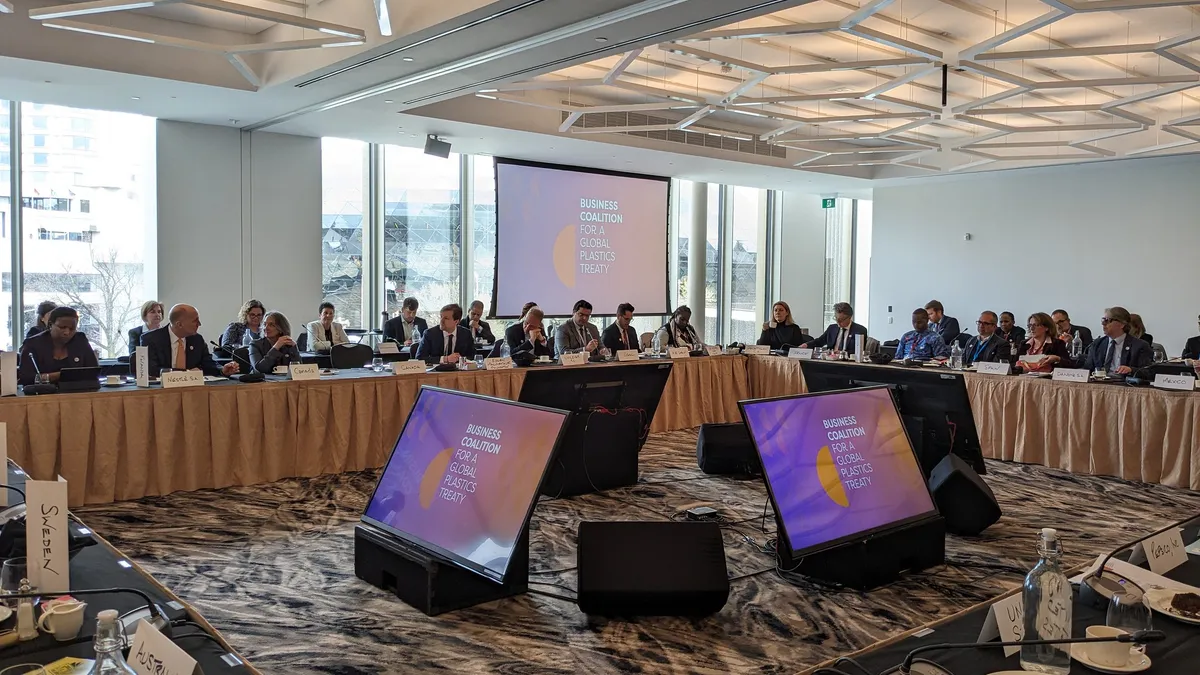 A room full of people in business attire, seated at multiple tables, discuss an international plastics treaty