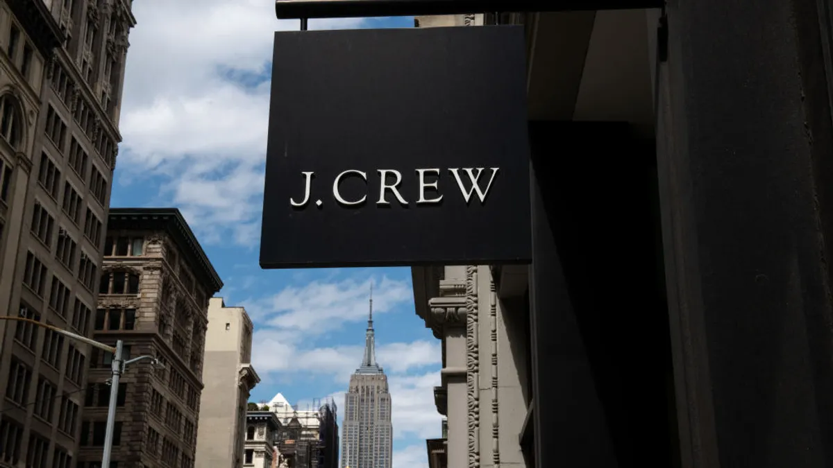 A black sign with the words "J. Crew" hangs from a building on a city street.