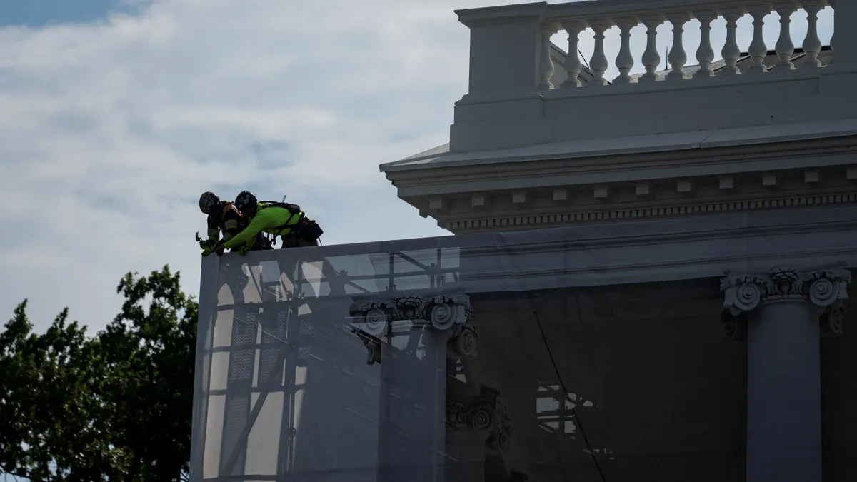 Two construction workers put tarp over scaffolding.