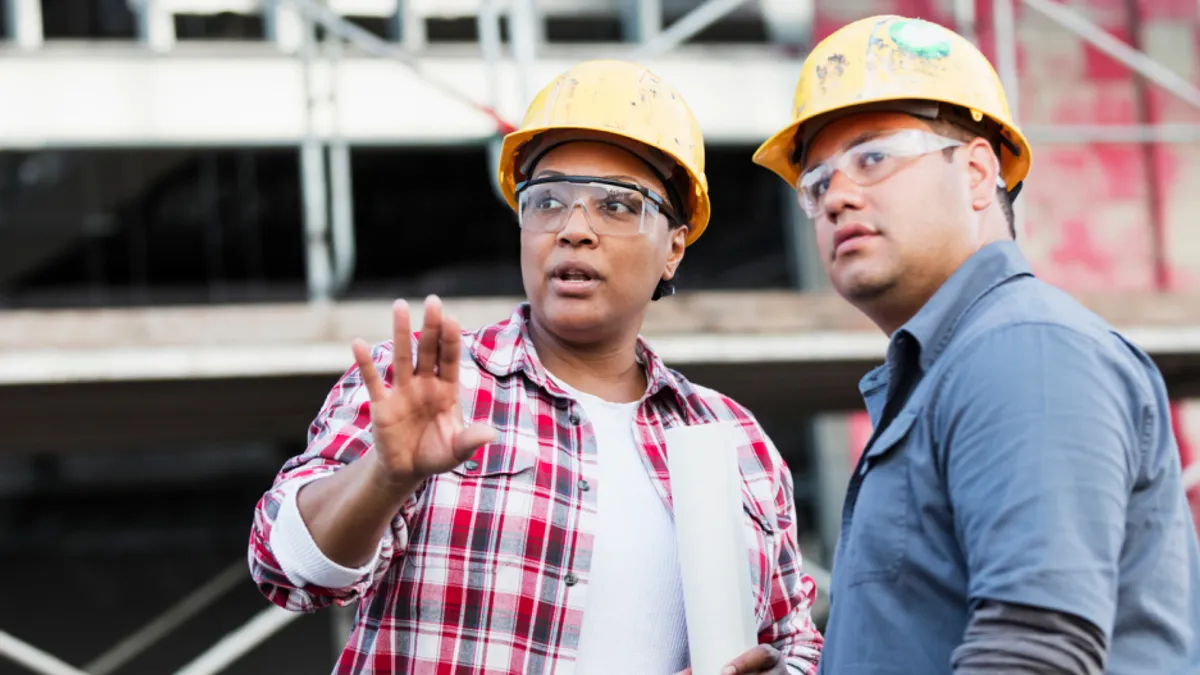 Two construction workers wearing hard hats discussing something