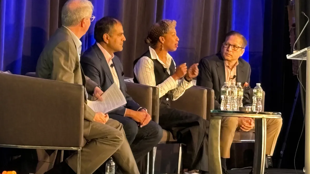 Three technology executives in business attire seated on a panel on stage