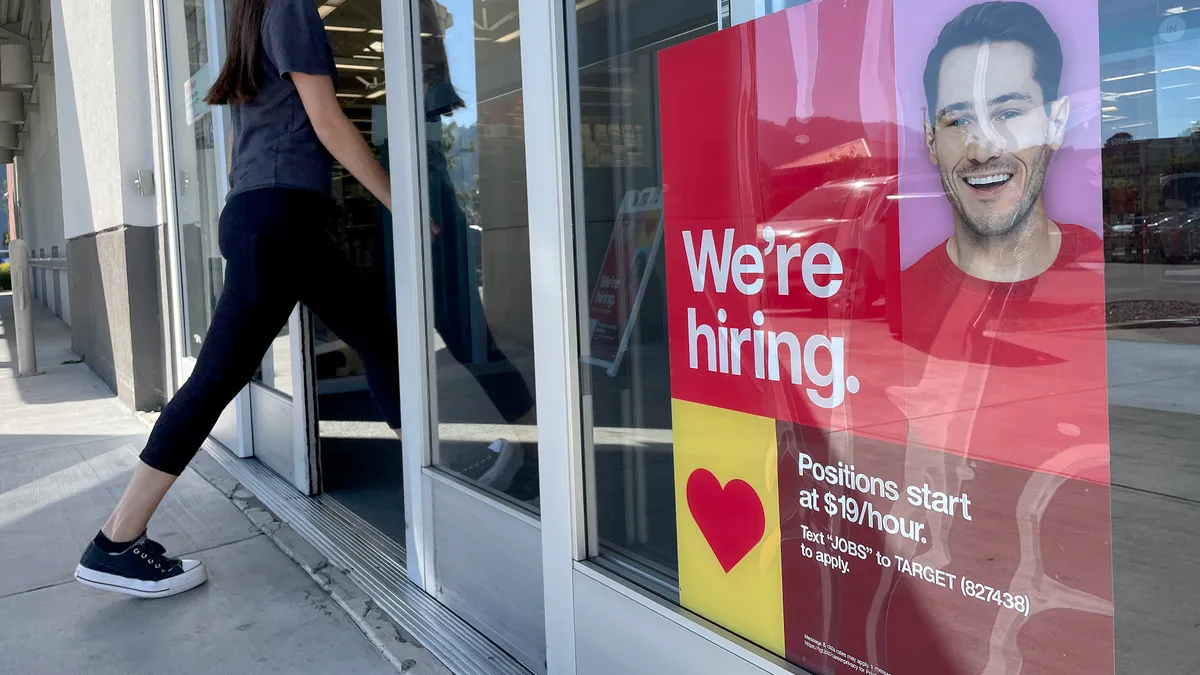 A person walks into a Target store, where a "we're hiring" sign is displayed.