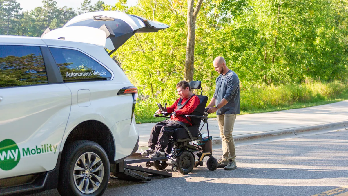 A man helps a person in a wheelchair up a ramp into a vehicle.