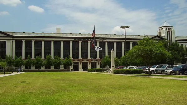 Low, wide building with columns and flags in front, with large lawn in foreground.