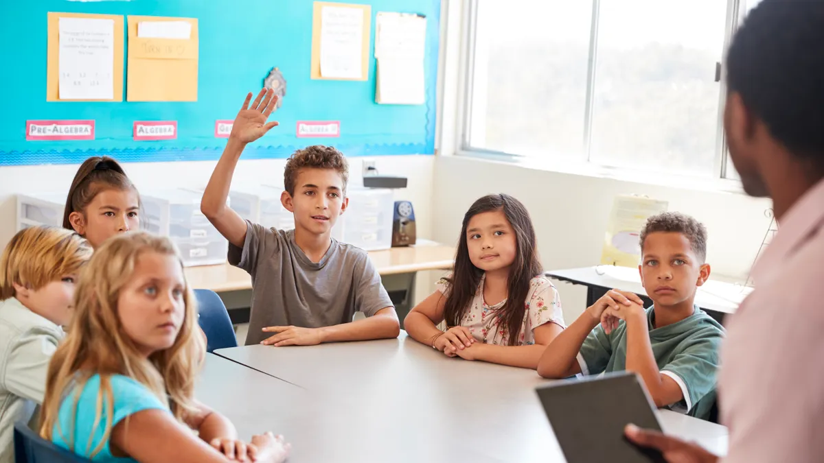 A young male student raises his hand to answer a question in an elementary school class.