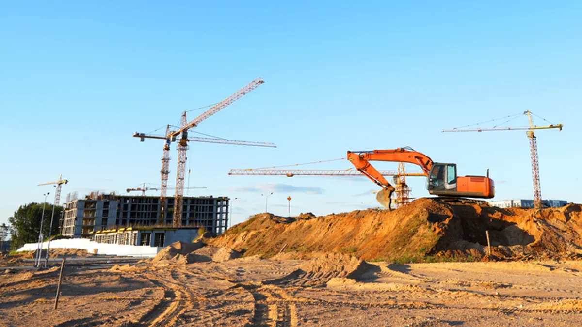 Large cranes tower over dirt and construction machinery on a jobsite.