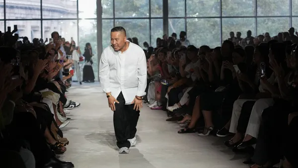 A person in a white shirt and black pants bows to the crowd while walking on a runway.