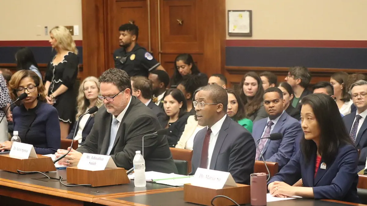 Four people sit at a table with microphones. Behind them are people seated in rows