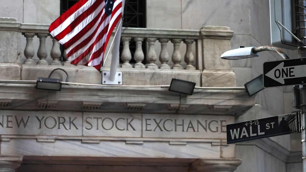 A flag hangs above a marble sign reading "New York Stock Exchange." In the foreground, a street sign identifies Wall Street.