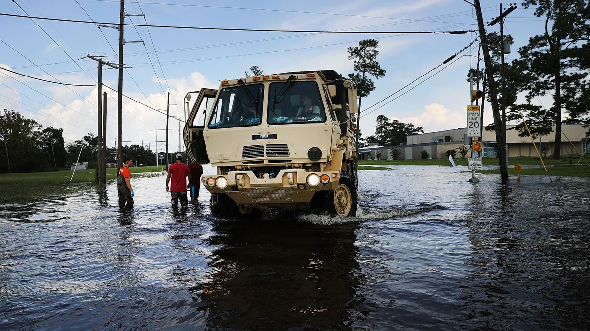 A large tan National Guard truck parked on a flooded street in Texas with three people standing alongside.