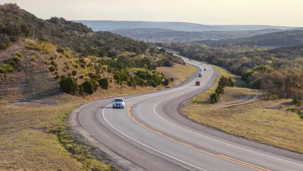 A winding road with a few cars through a hilly landscape.