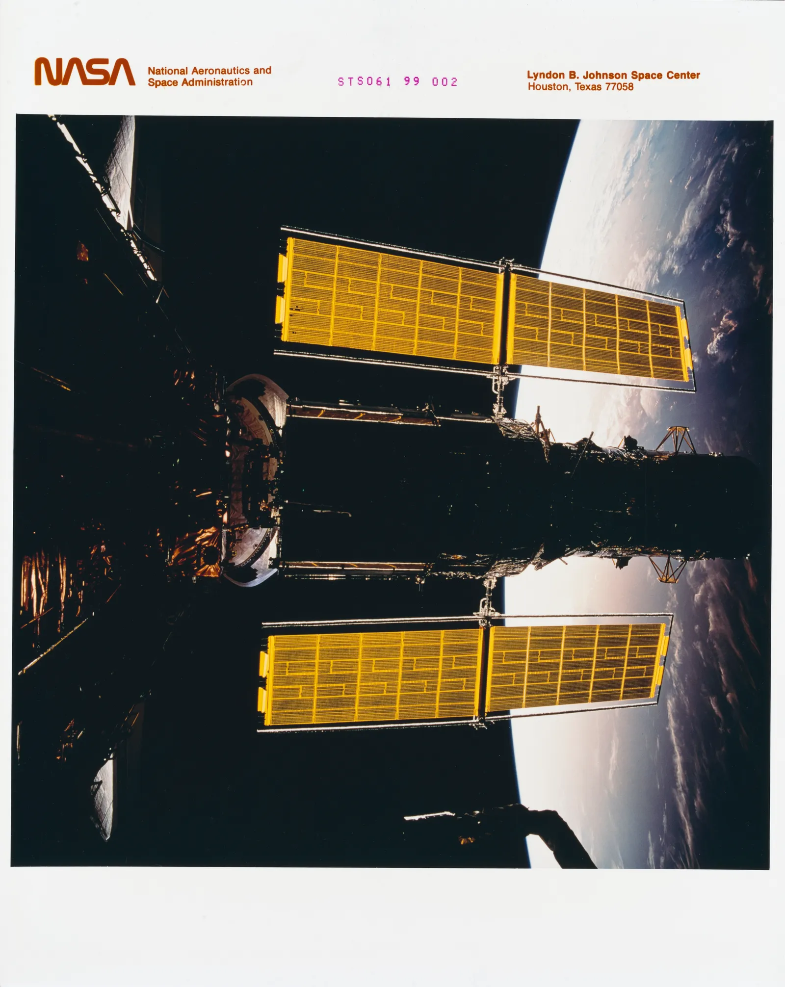 The new set of solar array panels deployed on the Hubble Space Telescope (HST) is backdropped against the blackness of space and a cloud-covered area on Earth.